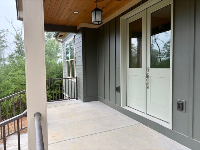 Covered porch with white French doors, gray siding, and metal railing overlooking trees