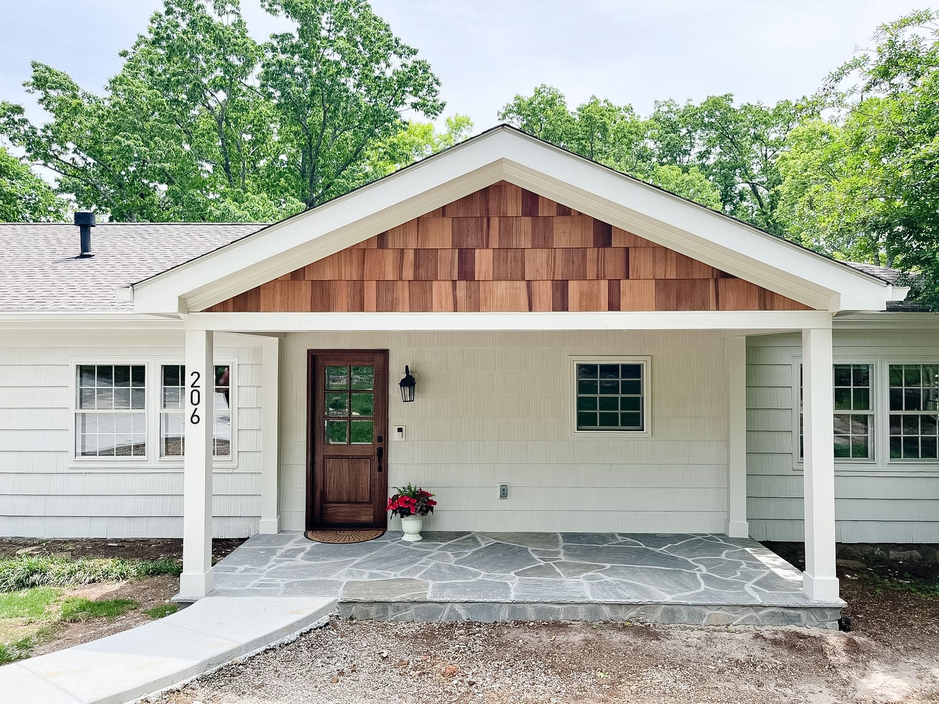 Front porch of a white house with a wooden gable and dark red front door