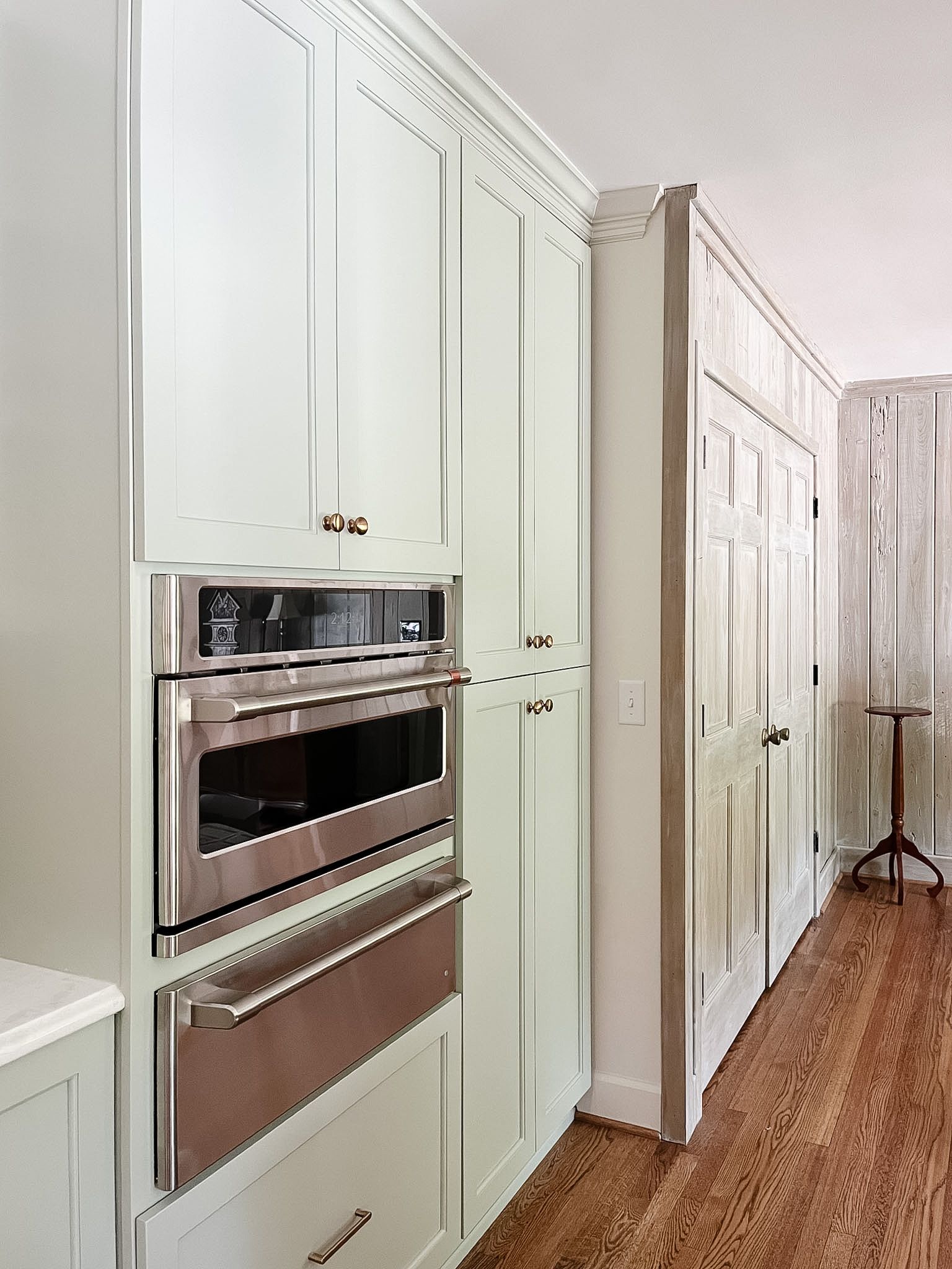 White built-in kitchen cabinets with a stainless oven and a hallway of white doors beside them