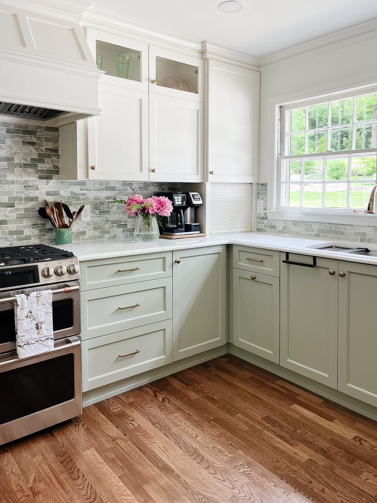 Bright kitchen with sage cabinets, white subway tile, stainless stove, and a window over a marble countertop.