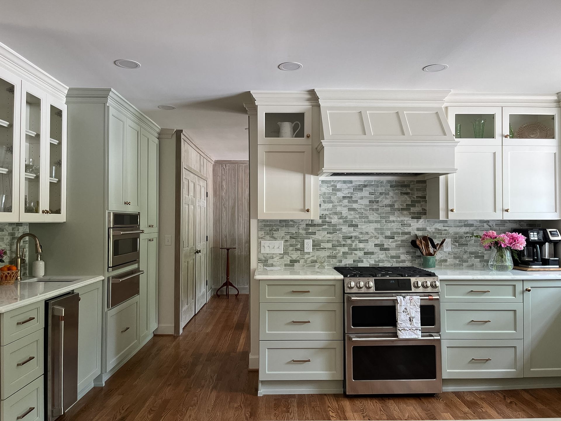 Bright white kitchen with stainless steel stove, pale cabinets, mosaic tile backsplash, and hardwood floor