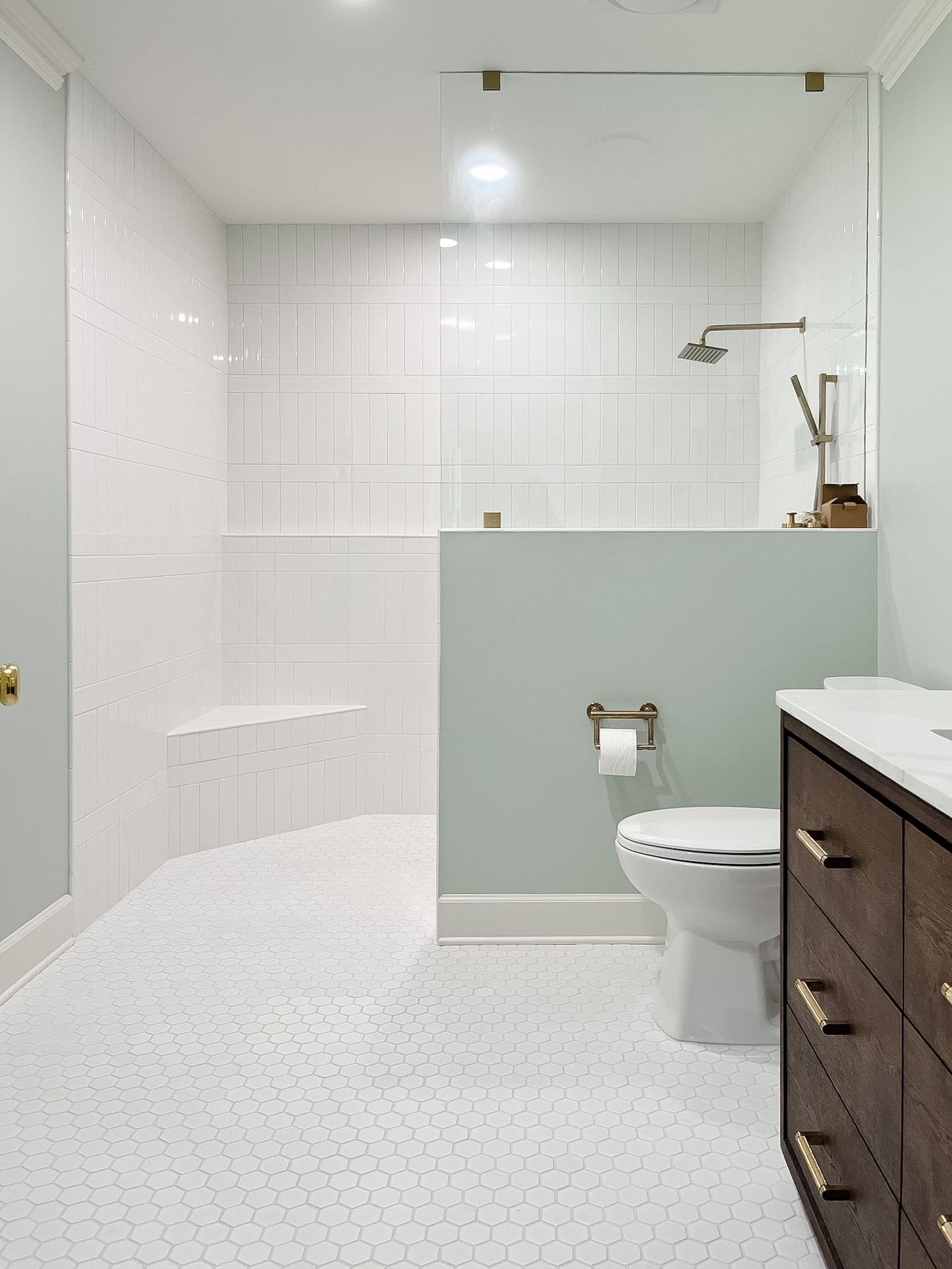 Bright modern bathroom with white tile, glass shower, toilet, and dark wood vanity