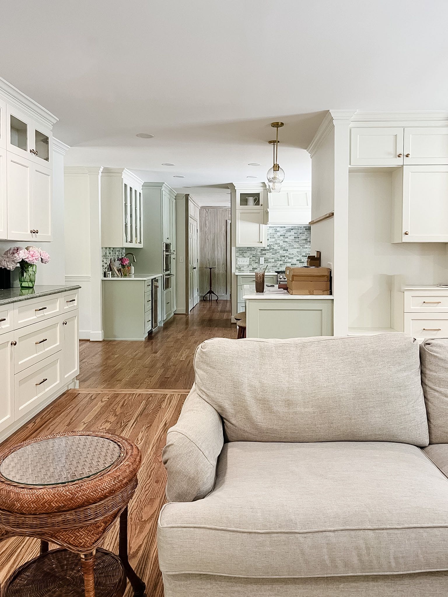 Bright white kitchen and living area with wicker chair and beige sofa in the foreground