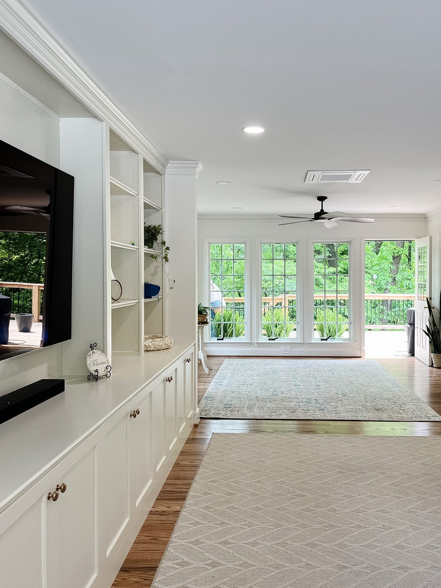 Bright living room with built-in cabinets, gray carpet, and large windows overlooking greenery