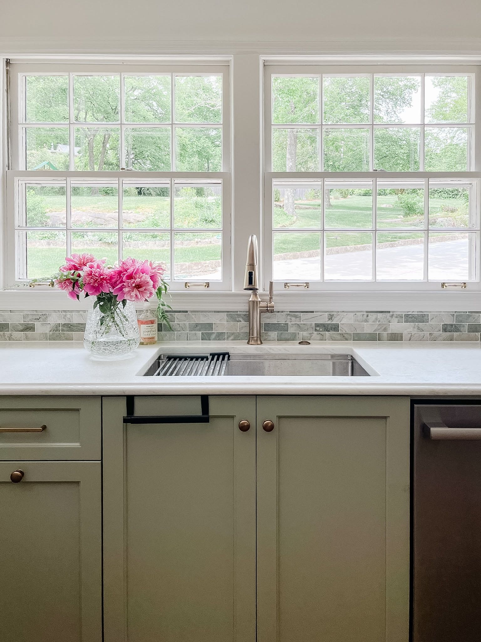 Bright kitchen sink beneath two windows, with pink flowers on the counter.