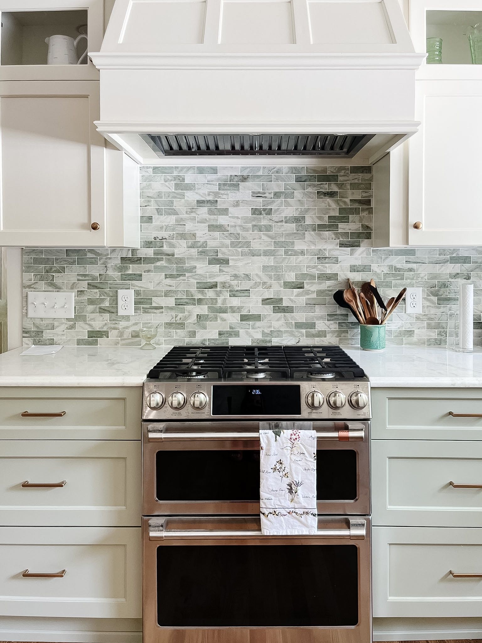 Modern white kitchen with stainless steel stove, mosaic tile backsplash, and white cabinets