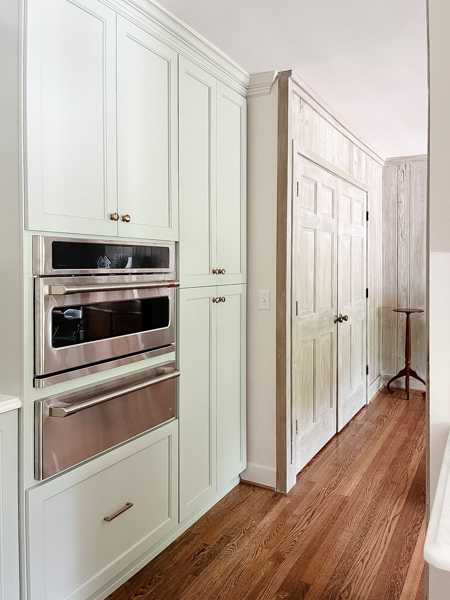 Bright kitchen hallway with white cabinets, built-in ovens, and wood floors