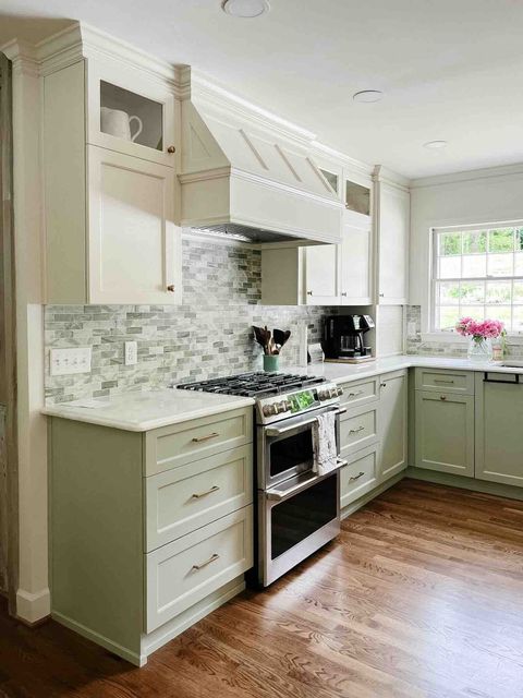 Green kitchen cabinets, stainless steel oven, white backsplash, and wooden floors.