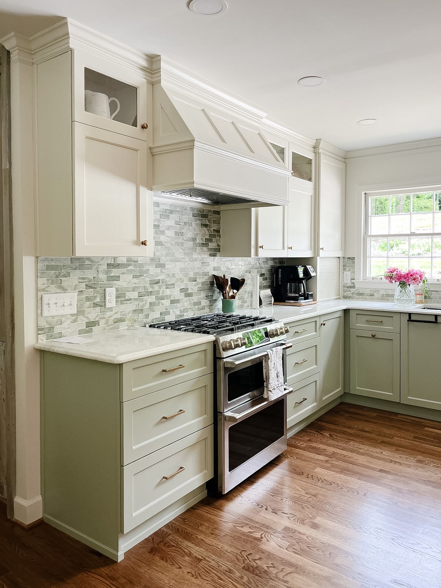 Bright kitchen with white cabinets, mosaic tile backsplash, stainless stove, and wood floors