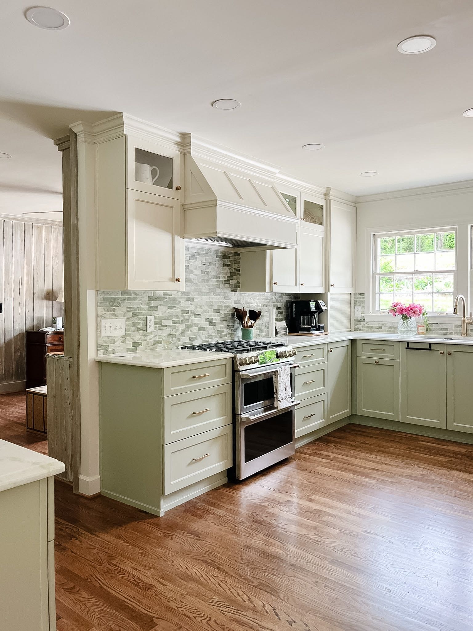 Bright kitchen with mint-green cabinets, white tile backsplash, hardwood floors, and a window over the sink.
