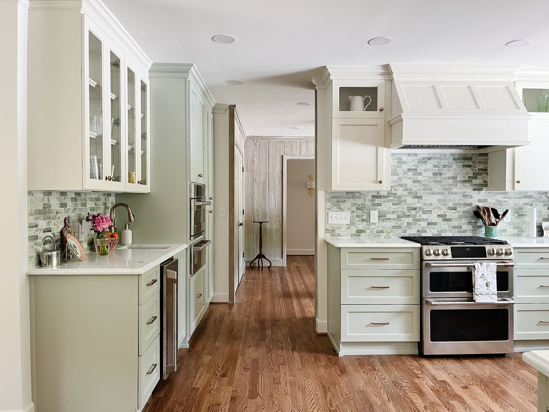 Bright white modern kitchen with stainless steel oven, glass cabinets, and wood floor