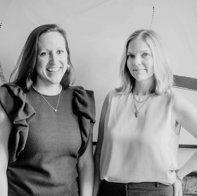 Two women smiling, posing indoors, one in a ruffle-sleeved top, the other in a sleeveless top.