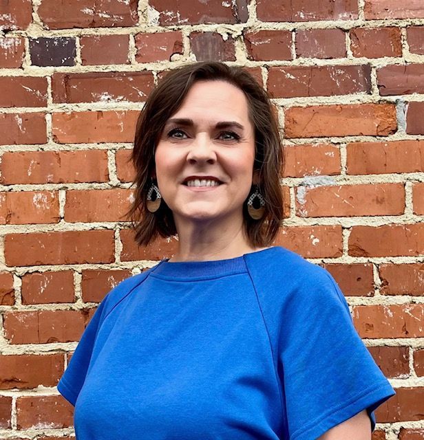 Woman in a pink shirt smiles in front of a weathered green background.