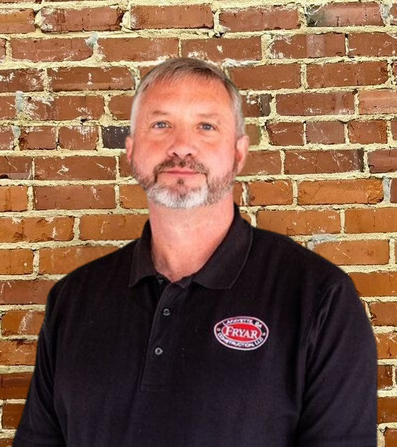 Man with graying beard in black shirt smiles, standing in front of a green background.