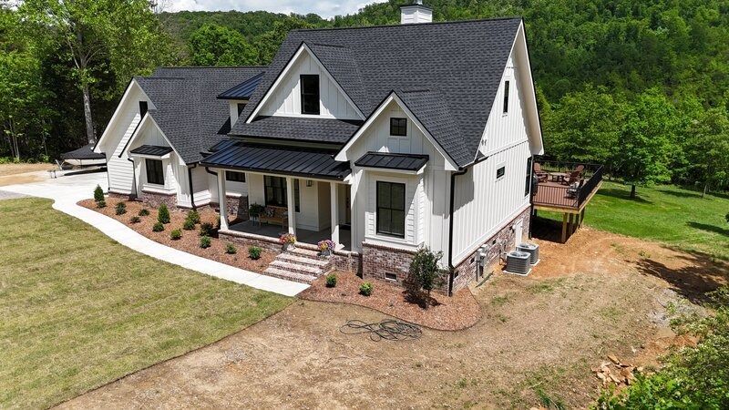 White farmhouse with black roof and trim, surrounded by green grass and trees.