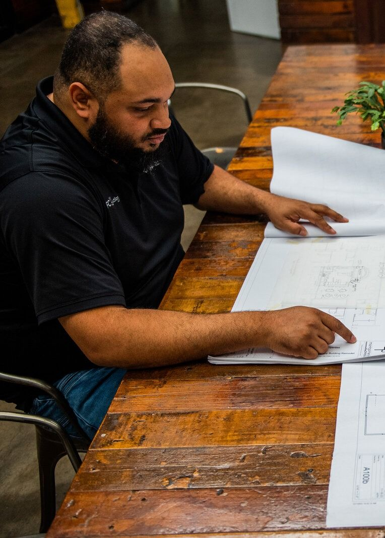 Two men review blueprints at a wooden table, discussing a project.