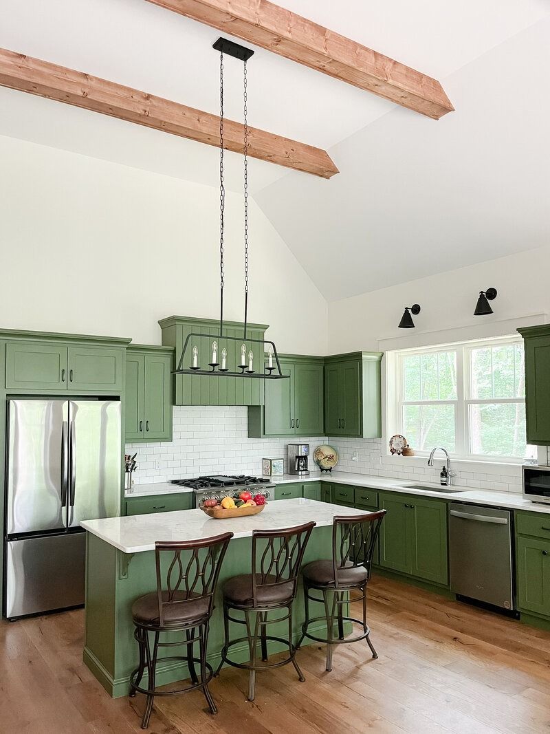 Green kitchen with white countertops, stainless steel appliances, and wood beams.