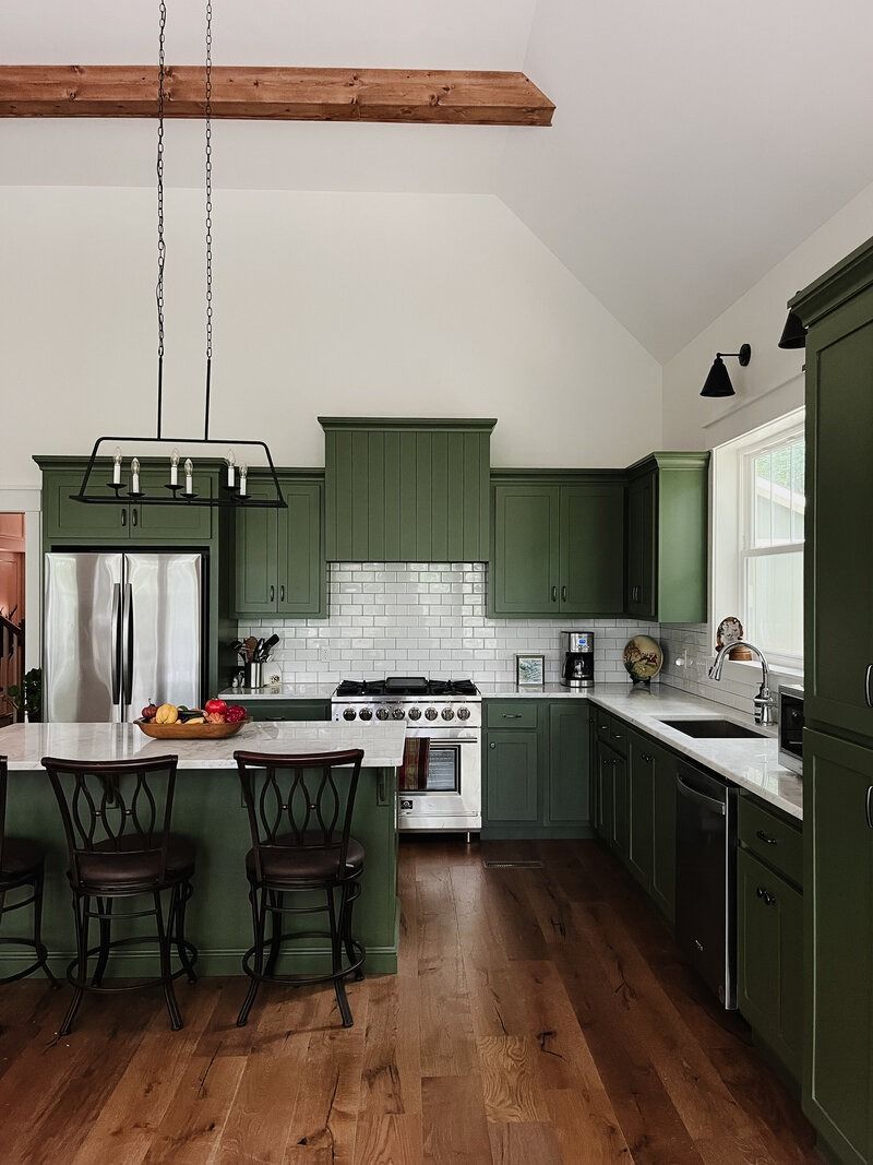 Green kitchen with stainless steel appliances, white countertops, and wooden floors.
