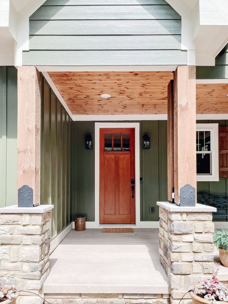 Green-painted porch entrance with a red door, stone pillars, and wooden ceiling.