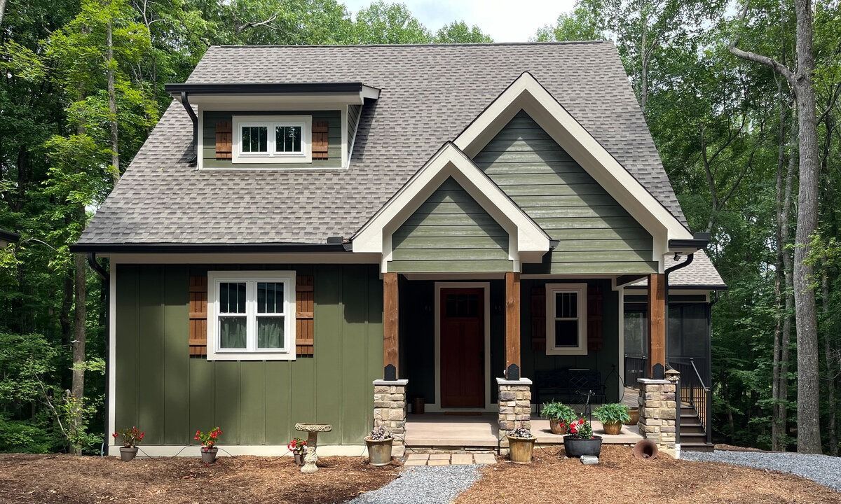 Green cottage with a brown roof and stone columns.