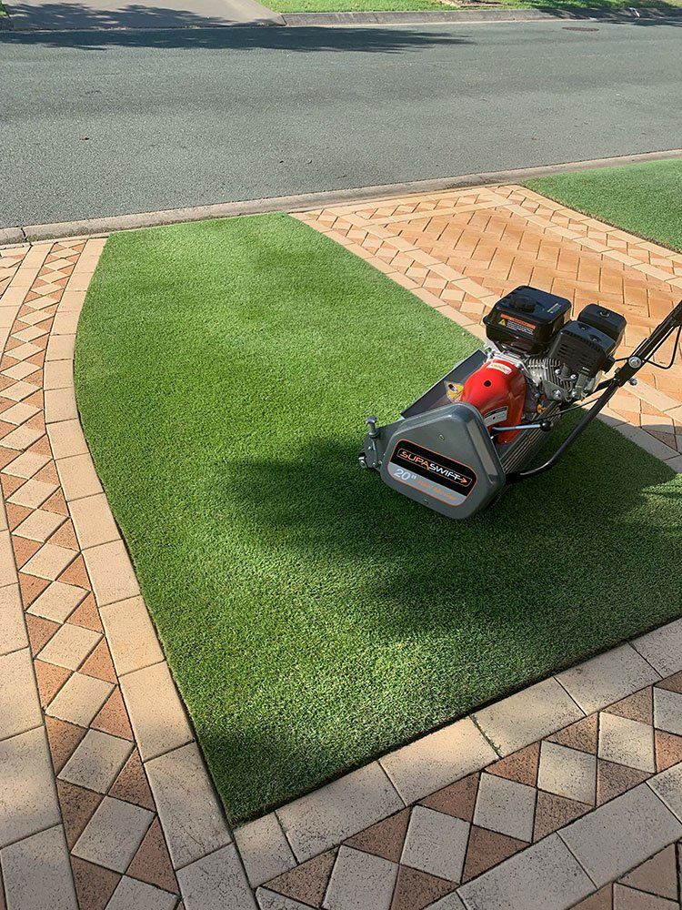 Red Lawn Mower on Artificial Turf Beside a Brick Driveway and Curb — Tweed Landscape Supplies in Tweed Heads, NSW