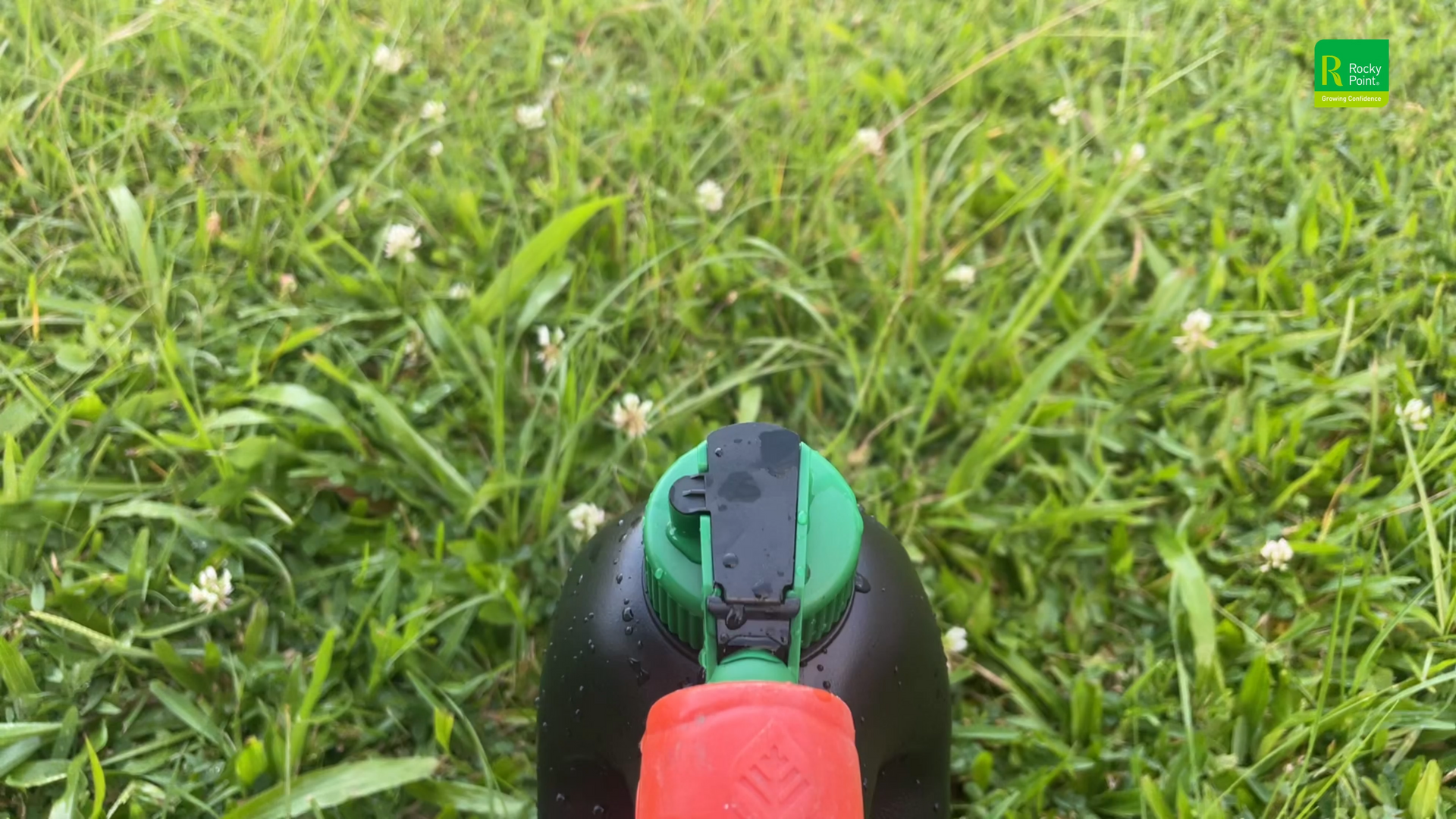 Red and Black Bottle Held Over Green Grass — Tweed Landscape Supplies in Tweed Heads, NSW