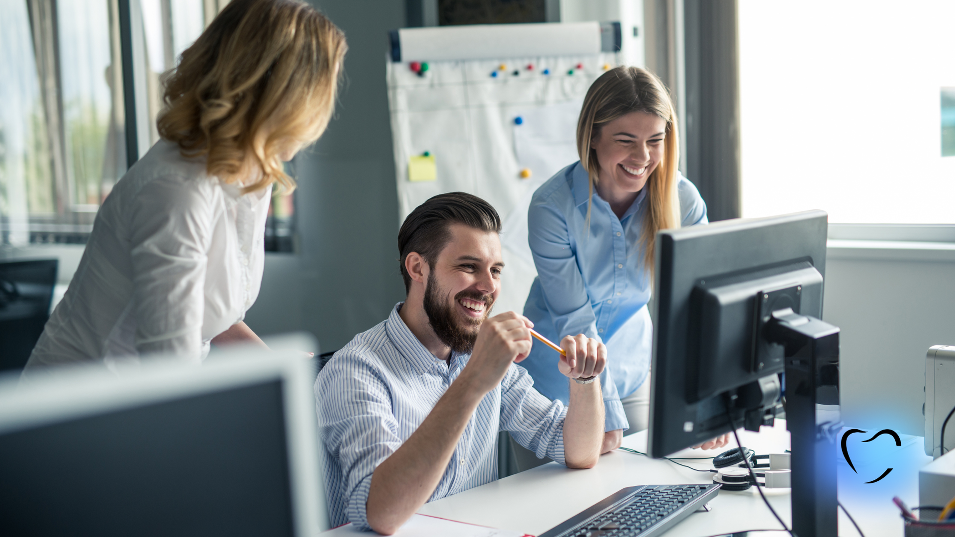 Three colleagues smile while collaborating on a project in a bright, modern office.