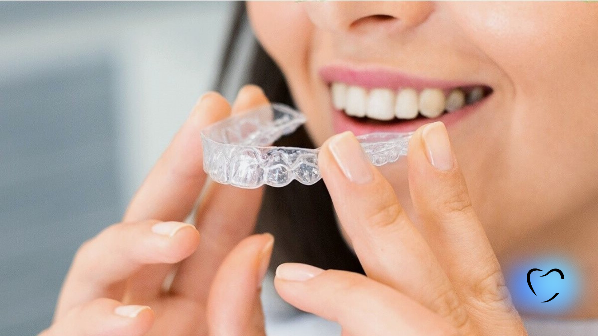A person holding a clear plastic orthodontic aligner tray up to their smile.