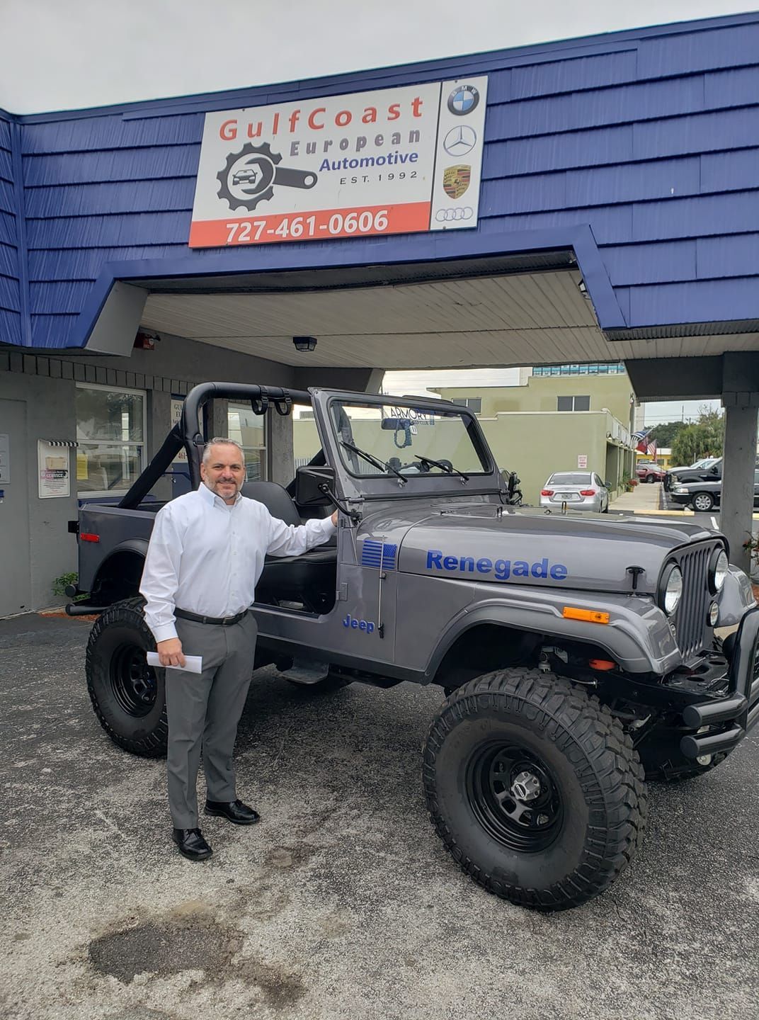 Man standing beside a gray Jeep under a Gulfcoast sign at an auto shop entrance | Gulf Coast European Automotive