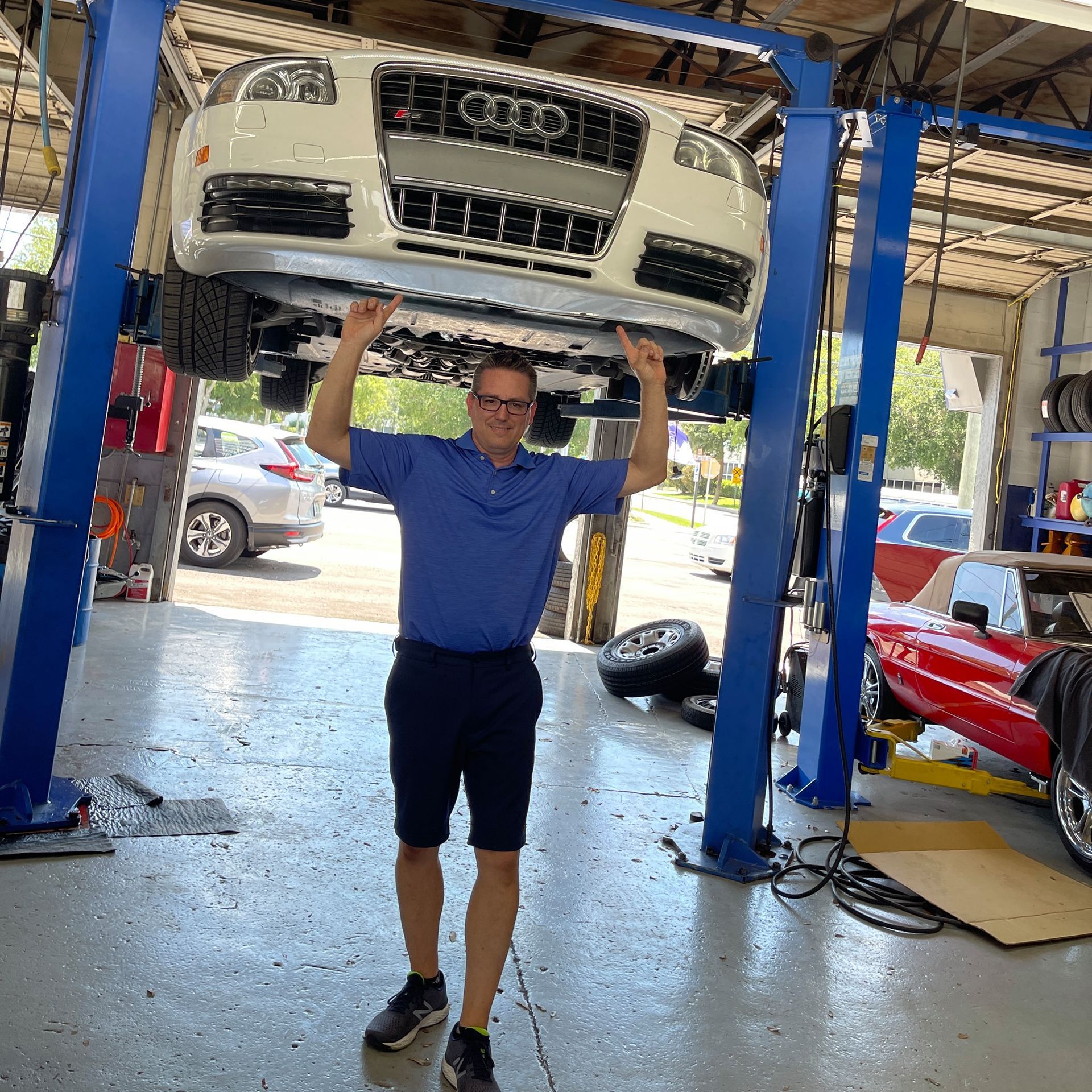 Man in blue shirt holding up a white Audi in an auto repair shop | Gulf Coast European Automotive
