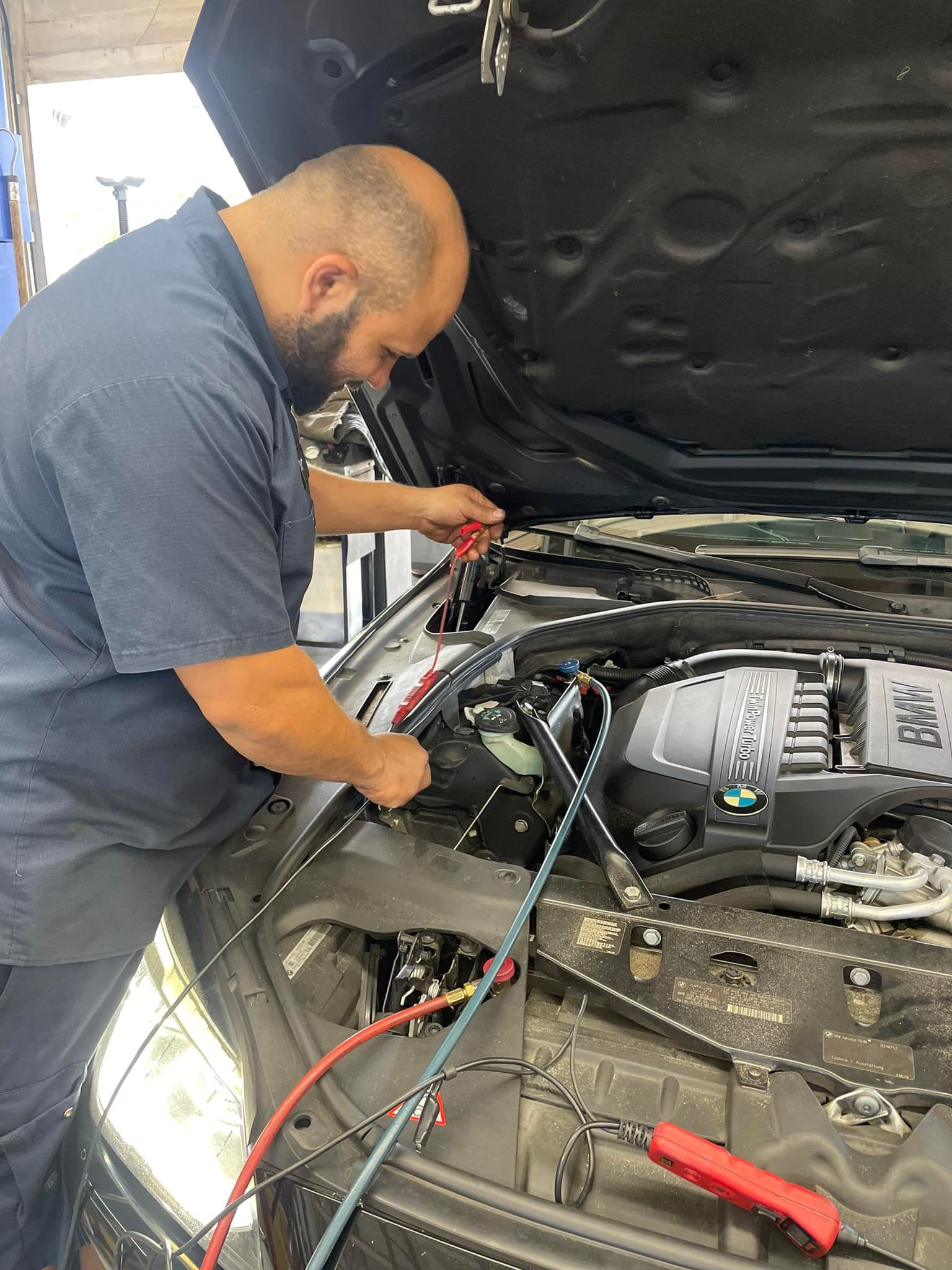 Mechanic using tools to work on a car engine under the open hood | Gulf Coast European Automotive