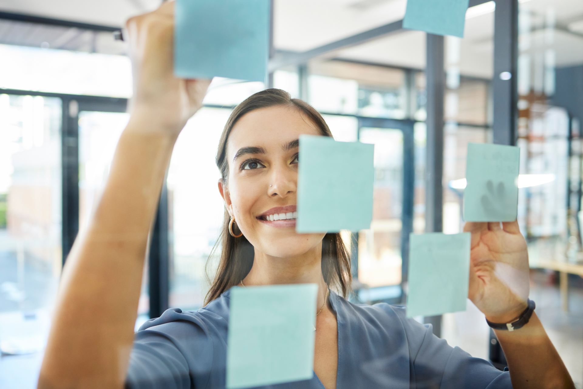 A woman is holding up sticky notes on a glass wall.