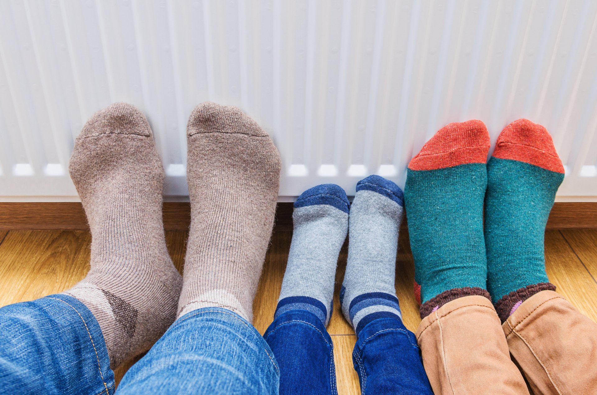 Quatre paires de pieds chaussés de chaussettes colorées reposent sur un parquet devant un radiateur.