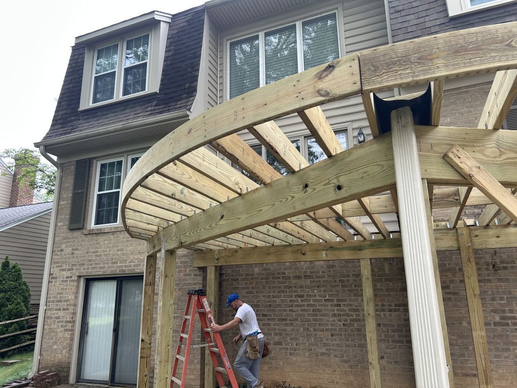 Worker on ladder building a wooden deck frame beside a brick house