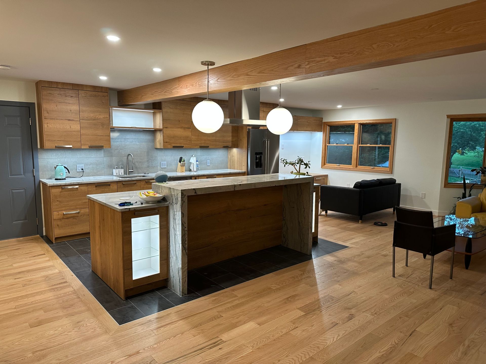Modern open kitchen and dining area with wood cabinets, island, pendant lights, and a living room corner