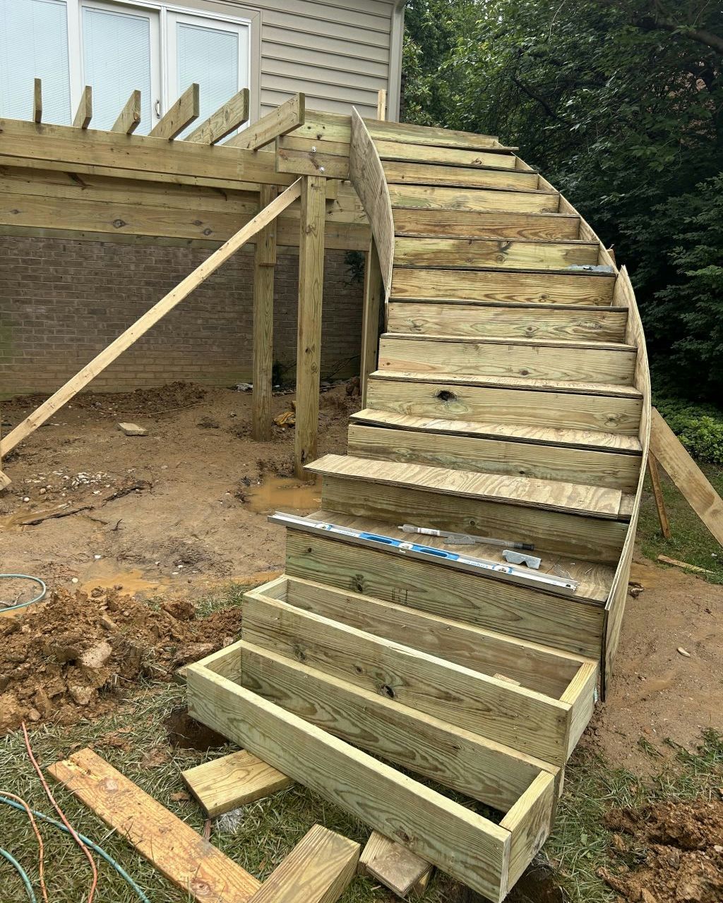 Curved wooden staircase under construction beside a house, with unfinished steps and support beams.