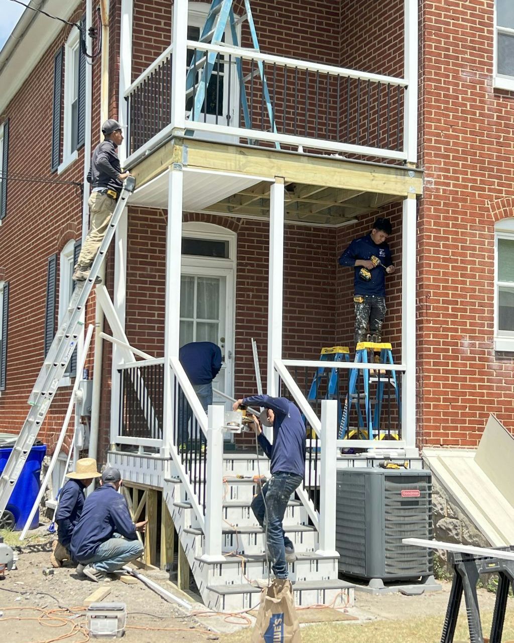Workers on ladders repairing the exterior of a brick building beneath a balcony.