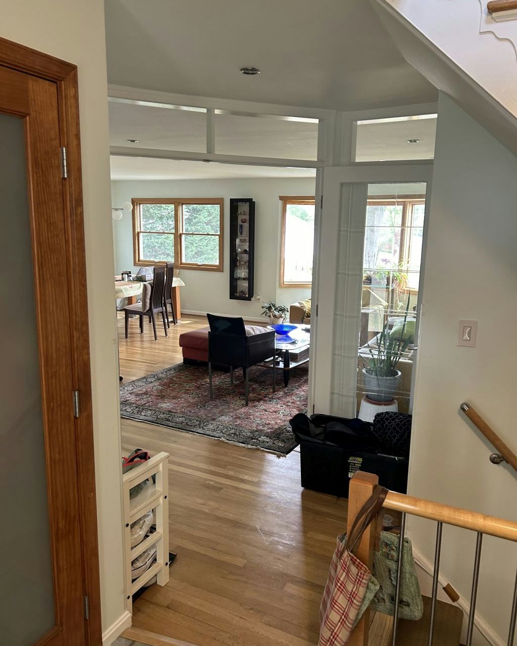 Bright living room with hardwood floors, large windows, and a patterned rug, seen from a staircase landing
