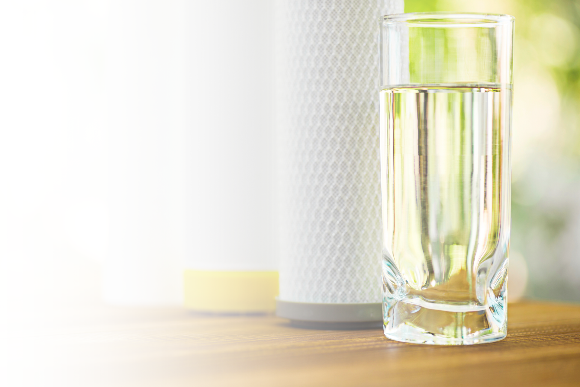 A glass of water is sitting on a wooden table next to a filter.