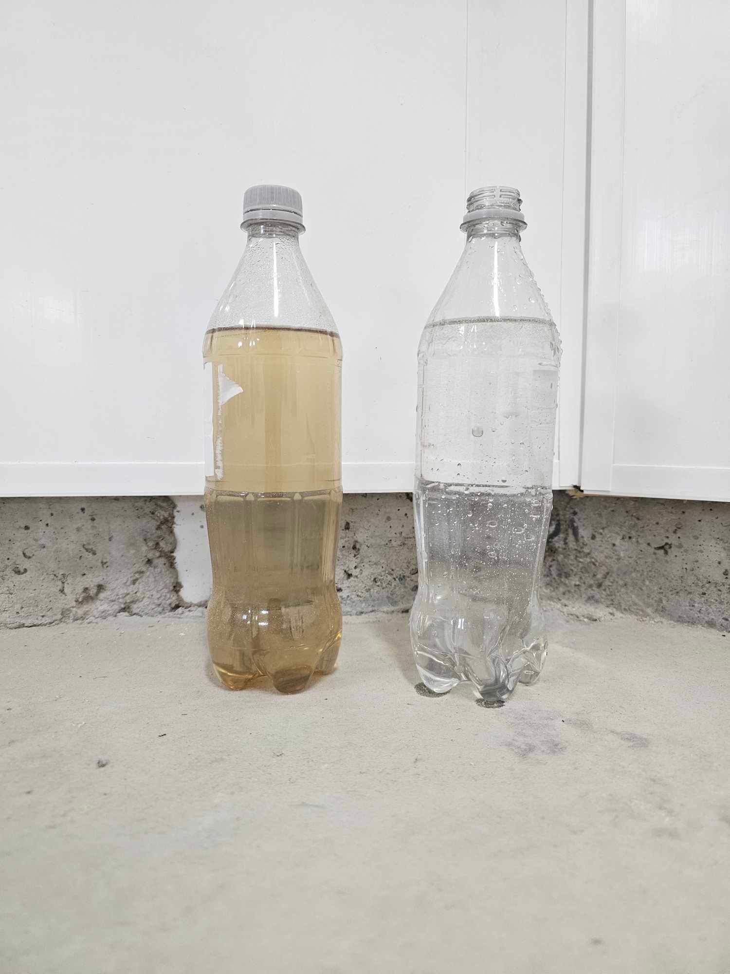 Two water bottles: one with murky brown water, the other with clear water, on a concrete surface.