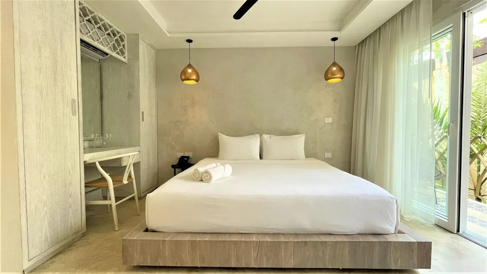 Bedroom with a bed, two lamps, a desk, and a large window with sheer curtains.