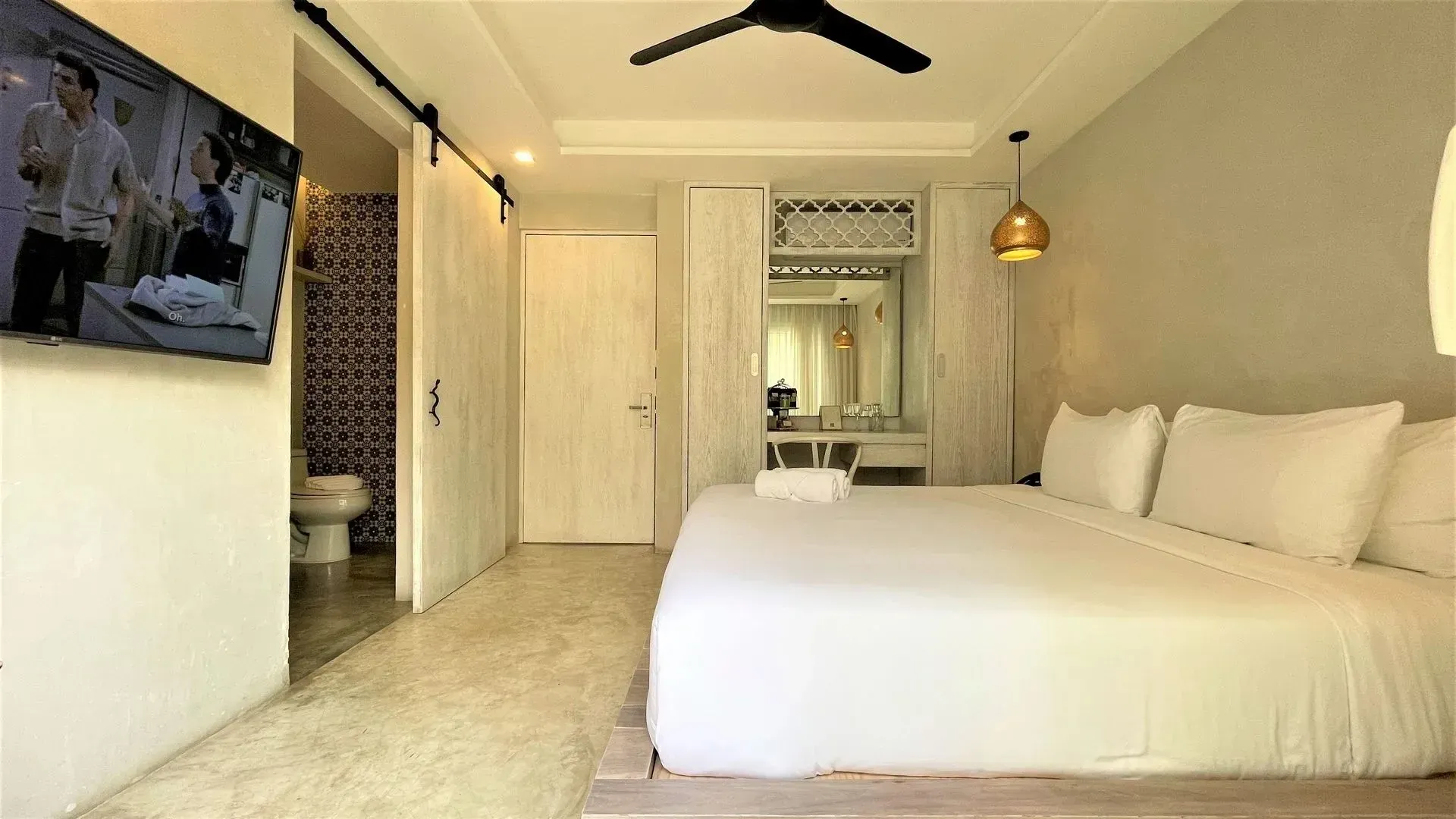 Bedroom with a large white bed, TV, bathroom, light walls, and a ceiling fan.