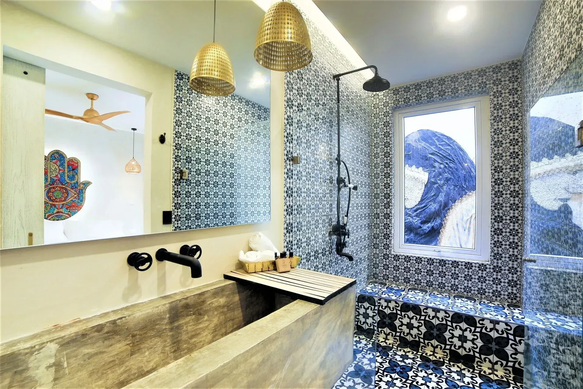 Bathroom with patterned blue and white tile, concrete sink, black fixtures, and gold pendant lights.
