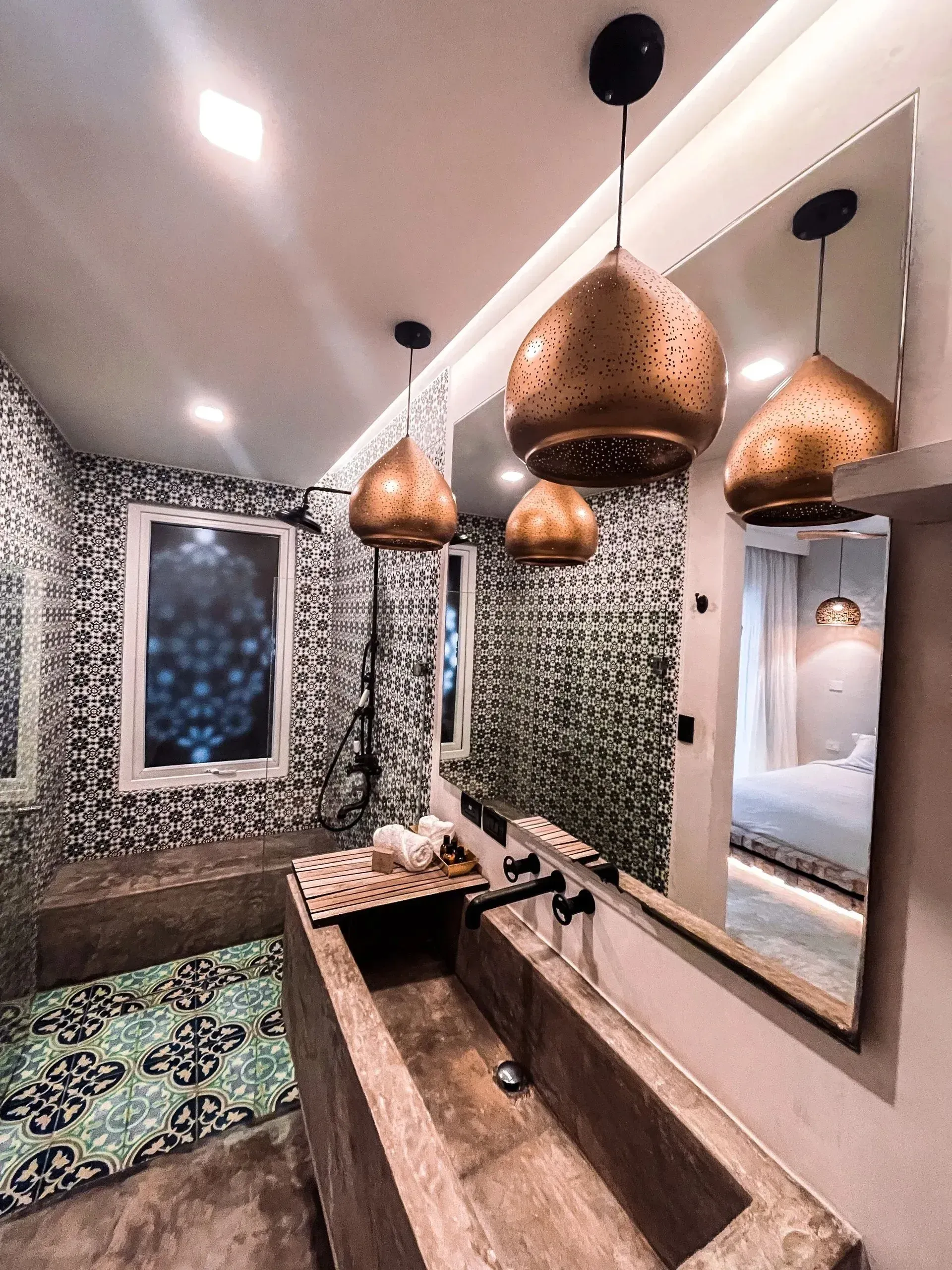 Bathroom with patterned tile, concrete sink, gold pendant lights, and large mirror.