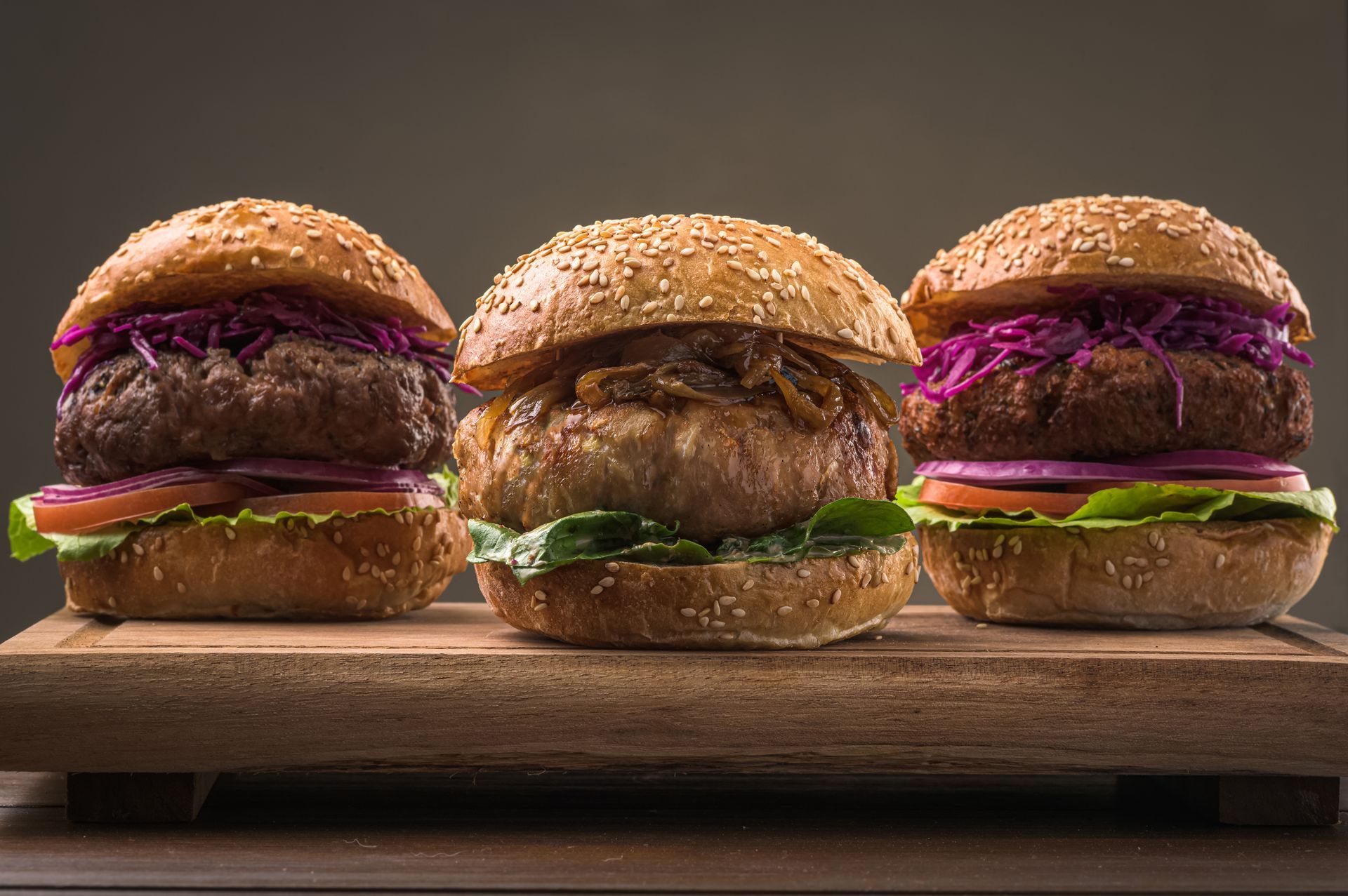 Three hamburgers are sitting on a wooden cutting board.