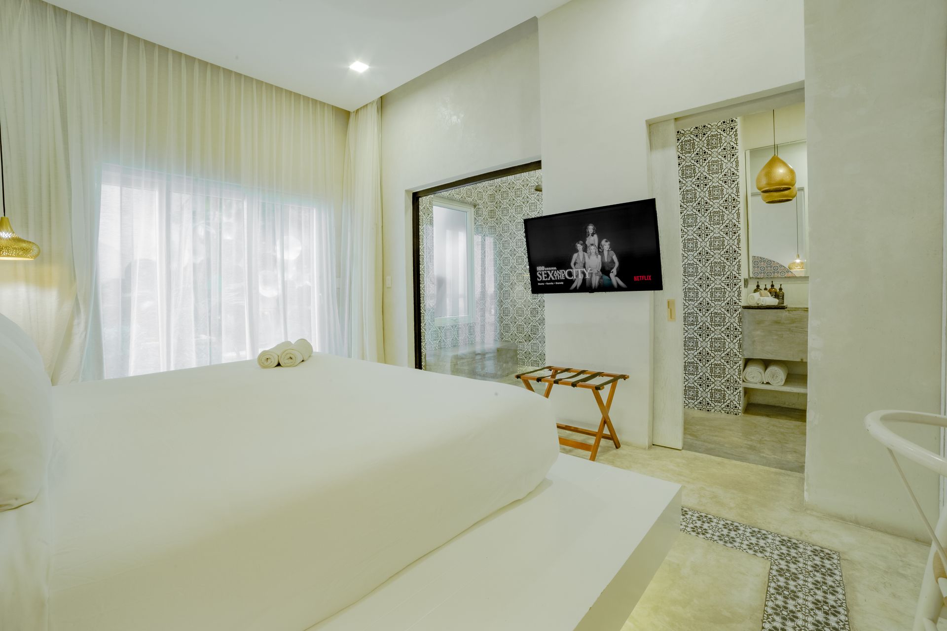 White bedroom with large bed, TV, and open bathroom.