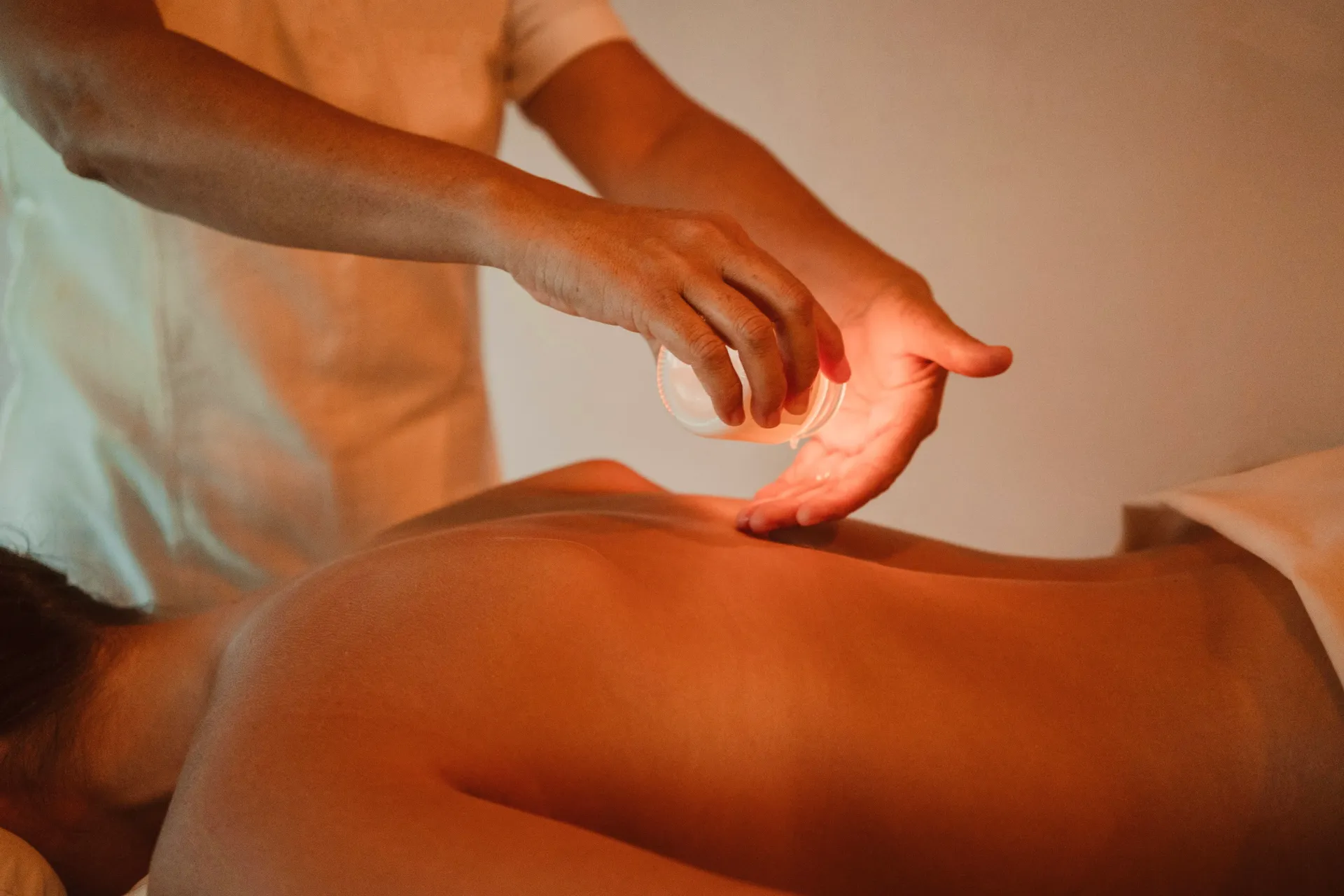 Person receiving cupping therapy on their back; hands hold the heated glass cup.