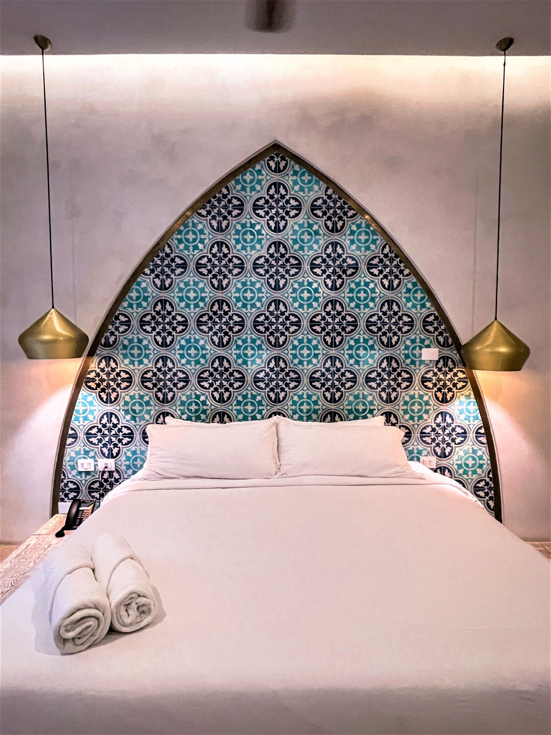 A bed with a patterned headboard and two towels on the bed.