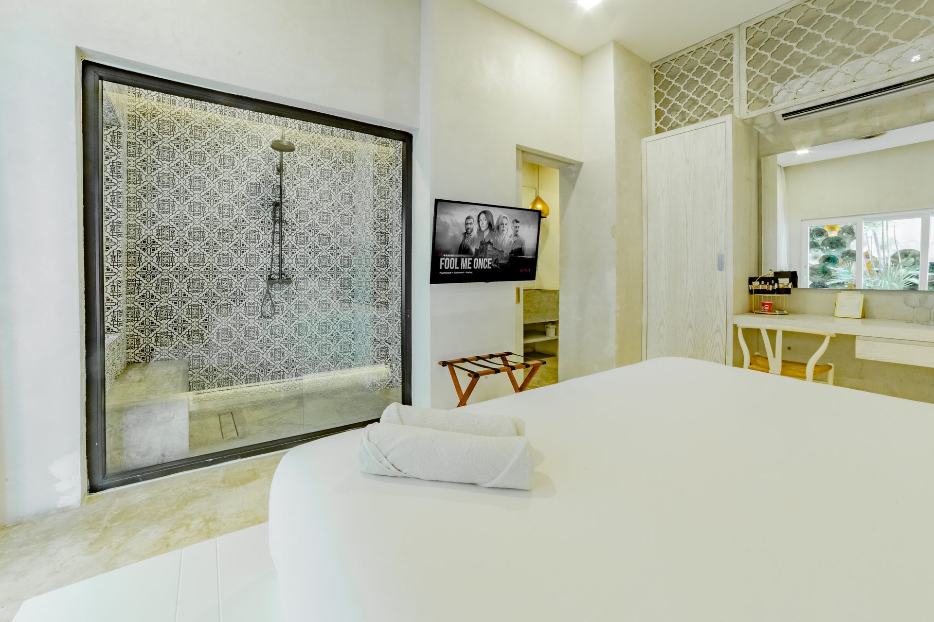Bedroom with white bedding, a glass shower, TV, and vanity.