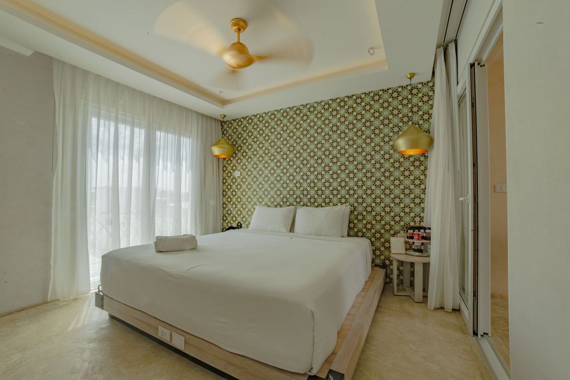 Dormitorio con una cama grande, pared con detalles estampados, cortinas blancas y ventilador de techo.